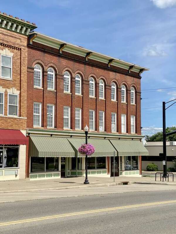 Built around the turn of the 20th Century, this Romanesque Revival and Italianate-style building features a red brick facade, bracketed cornice, low slope rear shed roof with a parapet, brick pilasters between the window bays, arched window bays not