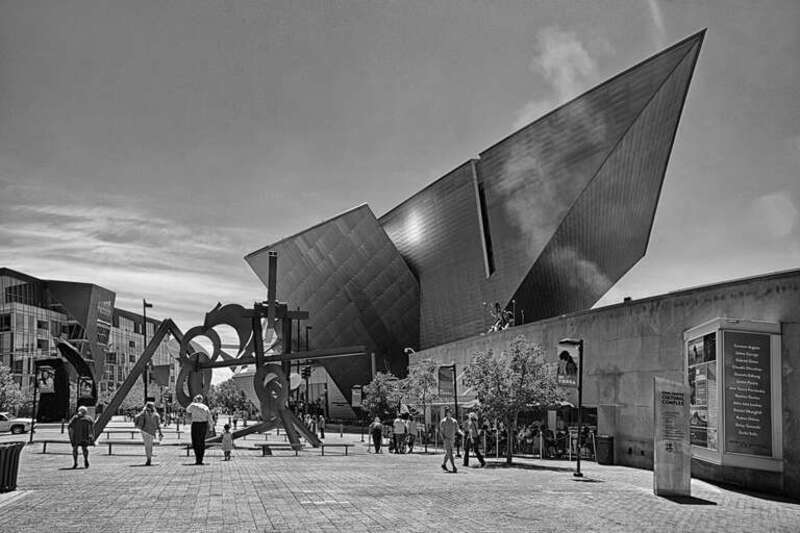 500px provided description: Pedestrians stroll along the Acoma Plaza of the Arts in the foreground. The unique geometry of the Denver Art Museum's Frederic C. Hamilton Building rises in the background. Smoke and steam billows from the chimney of the