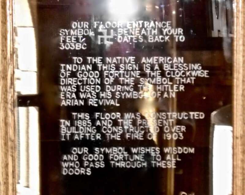 Doorway with etched glass description of the controversial counter-clockwise swastika mosaics on the floor of the building entryway, explaining the history and original intent of the design. Montana Club building, 24 W. 6th Helena, MT Built in 1905,