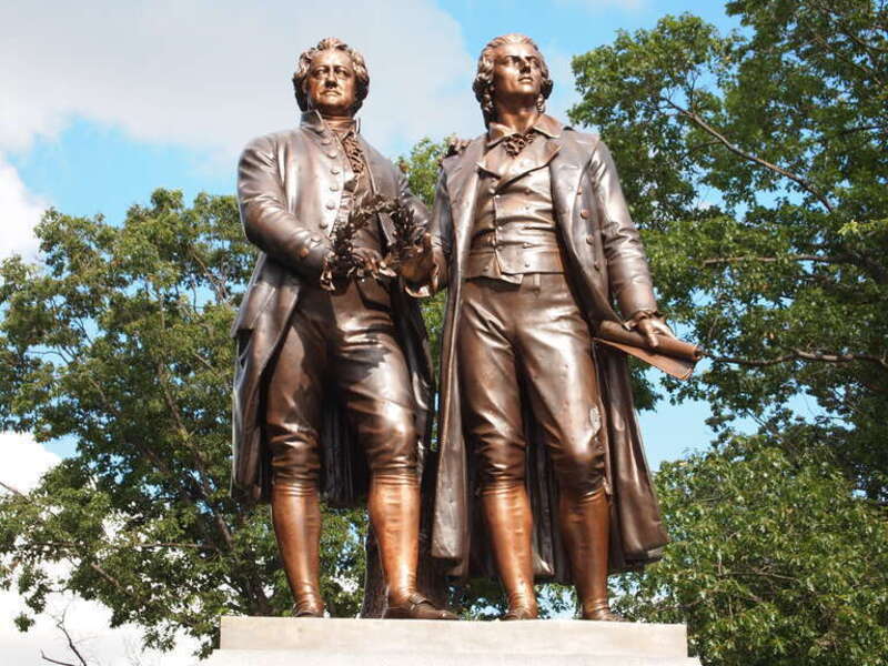 Photograph of the Goethe–Schiller Monument in Syracuse, New York (1911). Goethe is at the reader's left; he holds a laurel wreath in his own right hand, and is resting his left hand lightly on Schiller's shoulder. Schiller, to the reader's right, is
