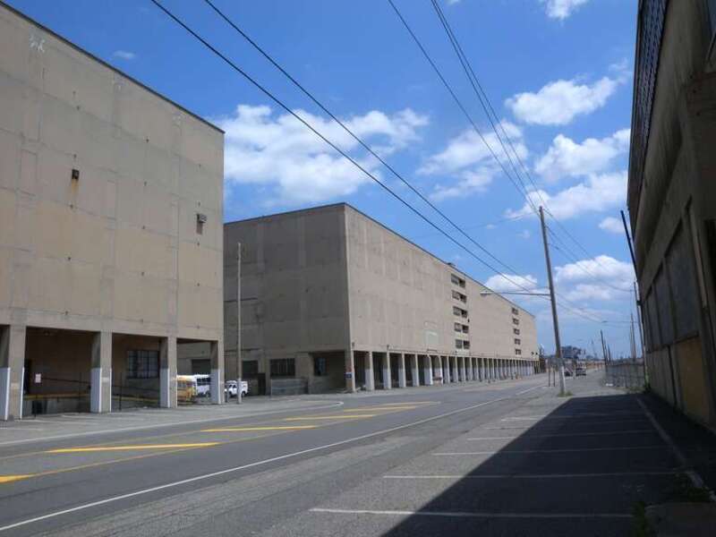 Looking east between warehouses on a hazy midday.  File:Bayonne Drydock &amp;amp; Repair jeh.jpg is in distant background.