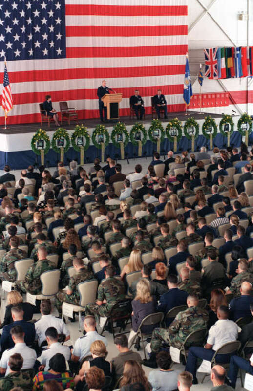 At a memorial service the 66th Rescue Squadron displays twelve wreaths with yellow roses and a photo of each airman killed in a helicopter accident.  The service is in the Thunderbird Hangar, Nellis Air Force Base, Nevada, while hundreds gather to