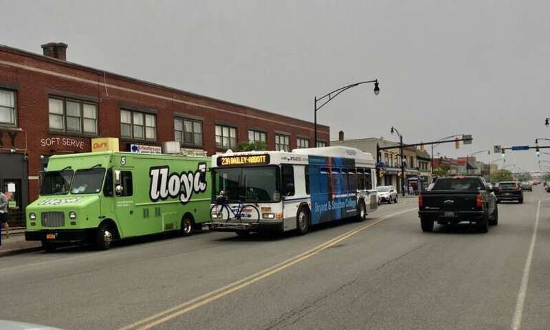 An NFTA Metro Bus on route 23 passes eastward through the bustling Hertel Avenue business district in North Buffalo on a dreary May 2021 evening. Its final terminus will be the bus loop at the corner of Bailey Avenue and Abbott Road, across from the
