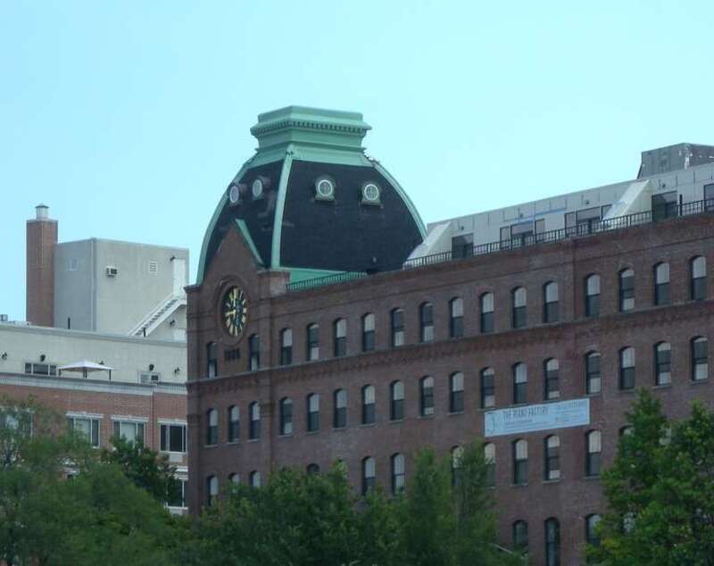 Looking east, full zoom, at Sohmer factory, now apartments, from Socrates Park on a partly cloudy midday.