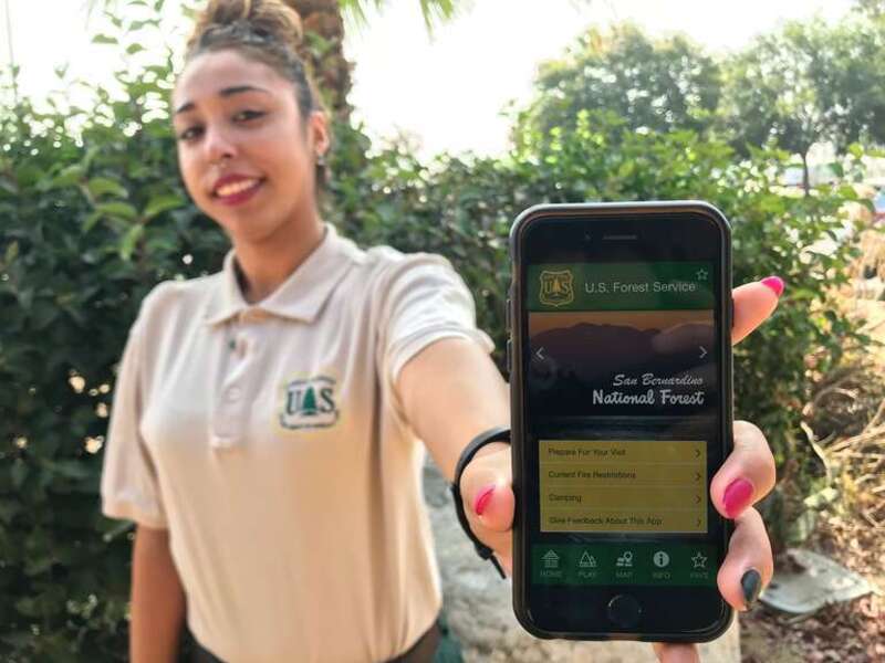 Visitor Service's Receptionist Rebecca Miller holds an iPhone displaying the landing screen for San Bernardino National Forest's first mobile app. 

(Forest Service photo by Zach Behrens)