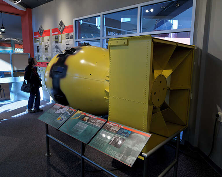 Jacki reads the Bradbury Science Museum's account of the history of World War II in Europe, next to a full scale model of the Fat Man atomic bomb dropped on Nagasaki, Japan.