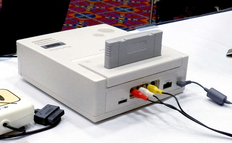 A rear view of the Nintendo Playstation prototype made by Sony for Nintendo's abandoned Super NES CD-ROM project. Three RCA connectors and a power cord are inserted in the rear, and a en:Super Famicom game cartridge is inserted in the slot on top.