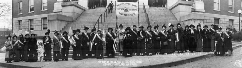 Panorama photograph of members of the Just Government League (this contingent known as Army of the Severn) [a women's suffrage organization], bearing banners and wearing sashes, standing before the steps of the main portico of the State House.