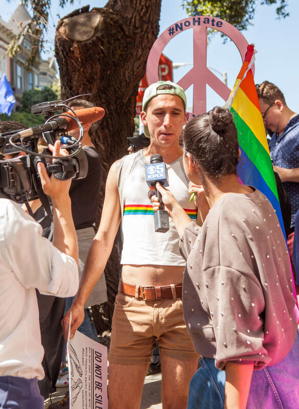 A protester holding a rainbow flag is interviewed by a KPIX Channel 5 reporter, at a Patriot Prayer counter-protest in San Francisco.