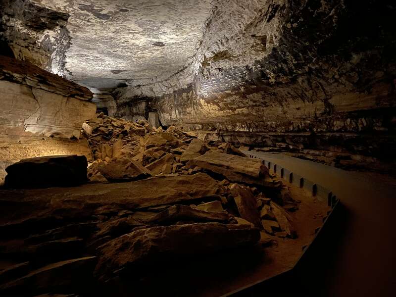 A paved trail winds its way through a large cave passage with large fallen rocks on the ground.
A paved trail winds its way through a large cave passage.