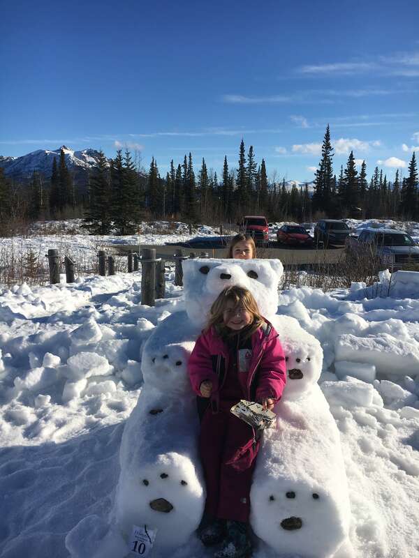 two kids pose by a snow block sculpted to look like a large bear
Winterfest in Denali