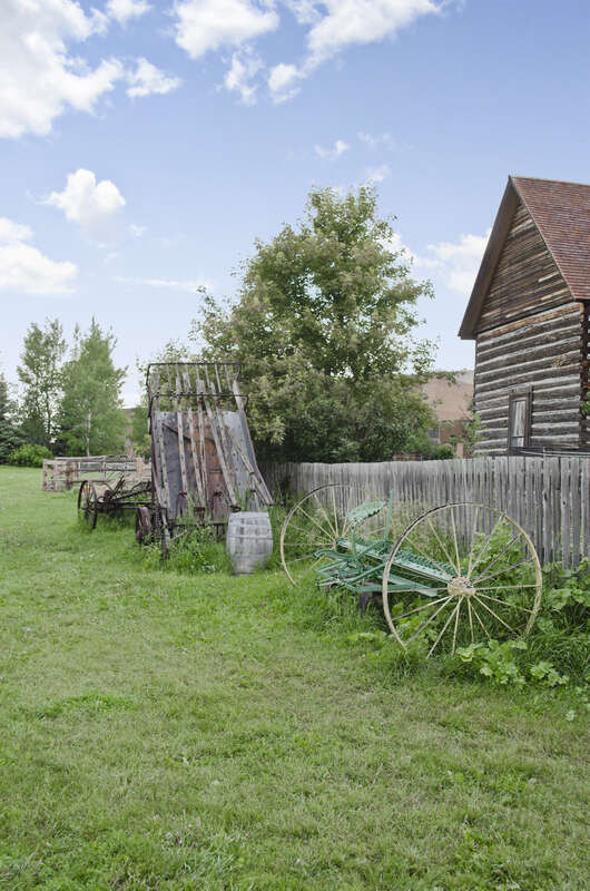 Agricultural implements on the grounds of the Tinsley Living Farm at the Museum of the Rockies in Bozeman, Montana.  These include a hay baler (the grey vertical piece), a seat rig (green axle with wheels), harvester, and plows.  The rig would be
