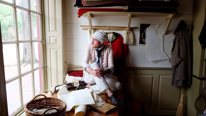 500px provided description: Man gazes out of window at Williamsburg. [#window ,#person ,#natural light ,#fabrics]