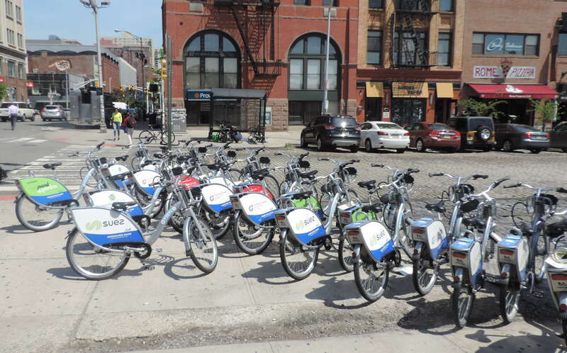 Looking north at Hudson Place station, with more Hudson Bike Share bikes than slots, on a sunny midday.