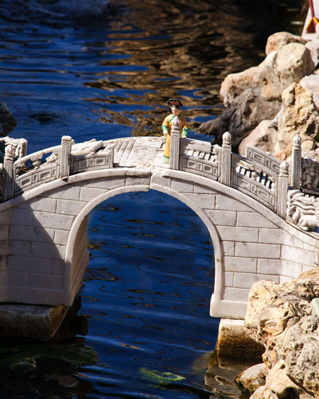 Miniature woman on a miniature bridge over a miniature river at Forbidden Gardens in Katy, TX