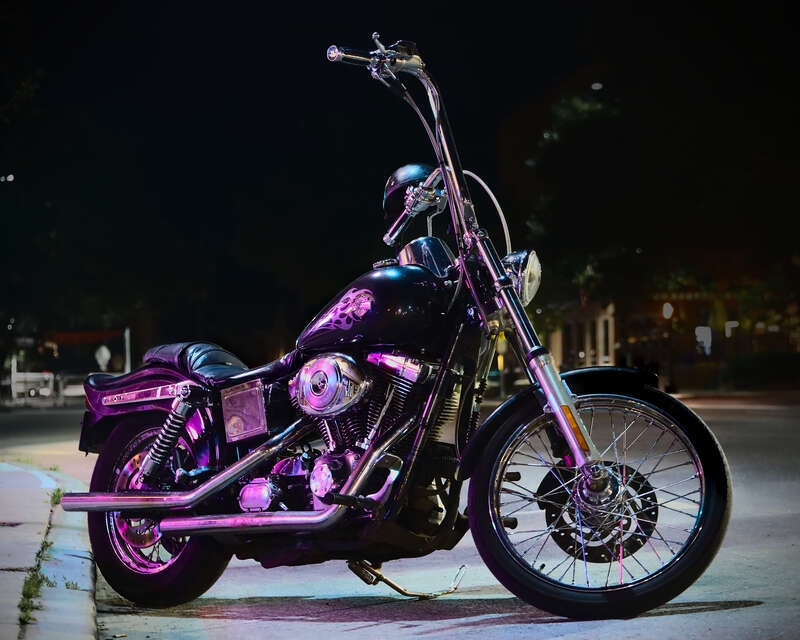 Harley-Davidson 2005 FXDWGI Dyna Wide Glide, with custom extra high &quot;ape hanger&quot; handlebars, on a dark street, illuminated by neon light of Charlie-O's World Famous dive bar in Montpelier, Vermont, United States.