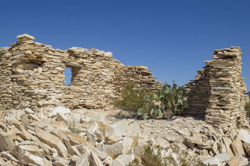 A collapsed portion of a house constructed of stacked limestone with a small window remaining, and the roof completely absent. A cactus grows inside.