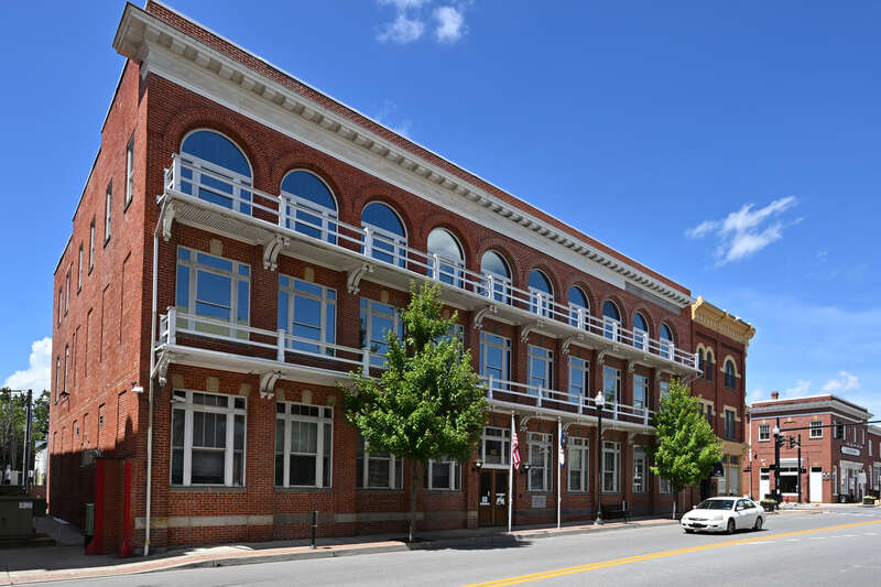 A three story brick building with large windows and a balcony running the length of the building on the second and third floors. 120 North George Street, Charles Town, West Virginia 25414.