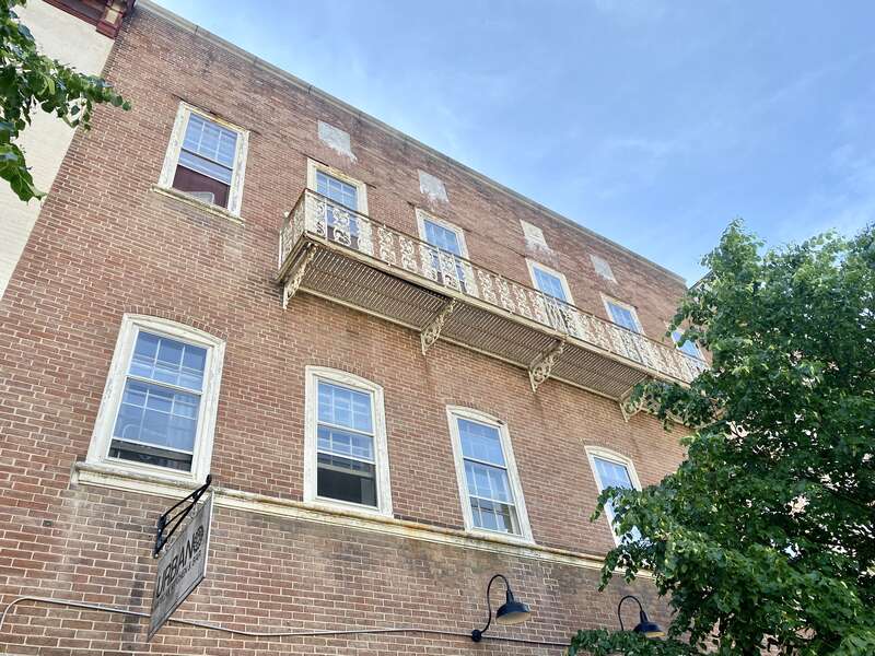 Built in the 19th Century, this building features a red brick exterior, nine-overnice and six-over-six double-hung windows, arches above the second floor windows, a cast iron balcony in the center of the front facade on the third floor, two first