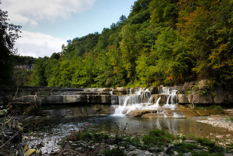 500px provided description: Walking on the pebbly river bank reaching Taughannock fall [#Nature ,#Fall ,#Forest ,#Wood ,#Water ,#Waterfall ,#NY ,#Ithaca ,#New York State]