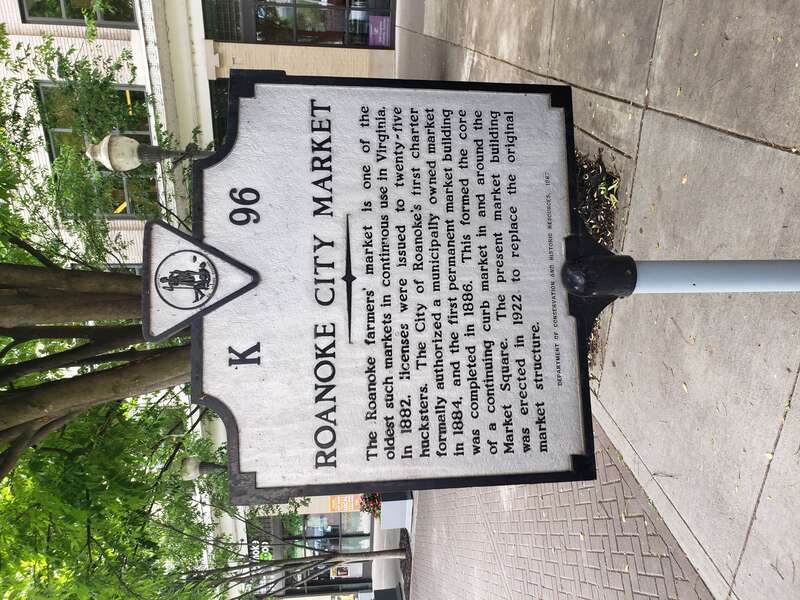 Sign outside the Roanoke City Market discussing its history. There is a tree in the background.