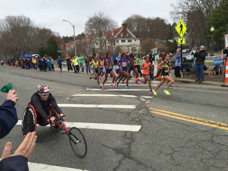 A group of nine women lead the race at Beaumont Avenue, Newton (mile 19), during the w:2015 Boston Marathon. Eventual winner w:Caroline Rotich is on the left. w:Bizunesh Deba leads followed by w:Mare Dibaba. A wheelchair participant is racing in the