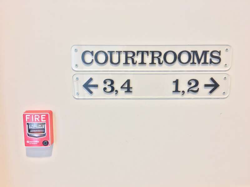 A sign in the Hillsborough County Superior Courthouse showing courthouse participants the direction on their courtrooms. There's also a fire alarm included in the picture.