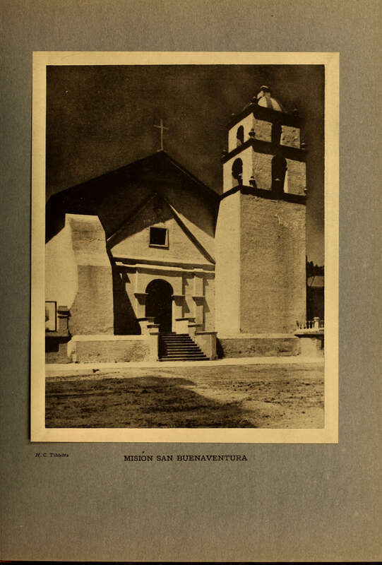 Sepia toned photograph of a adobe catholic mission with bell tower to the right and main building center-left, topped by cross.