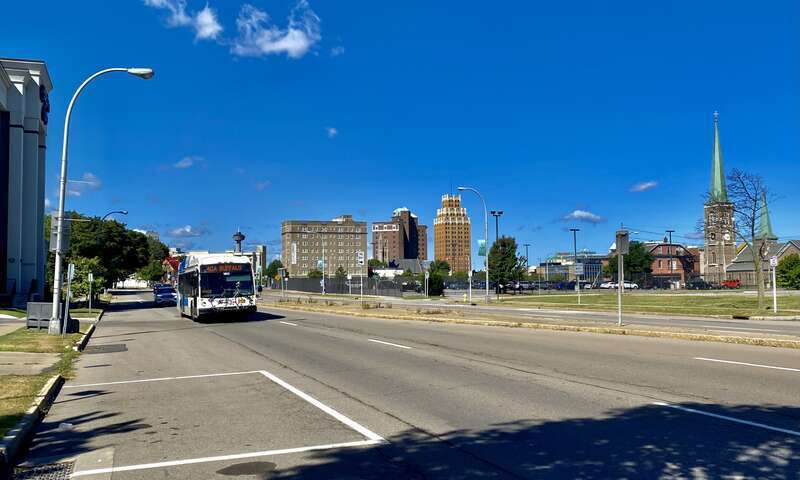As seen on a sunny September 2021 morning, an NFTA Metro Bus on route #40 proceeds eastward along Rainbow Boulevard past the Hampton Inn hotel as the skyline of downtown Niagara Falls, New York rises in the background. The bus is headed for downtown