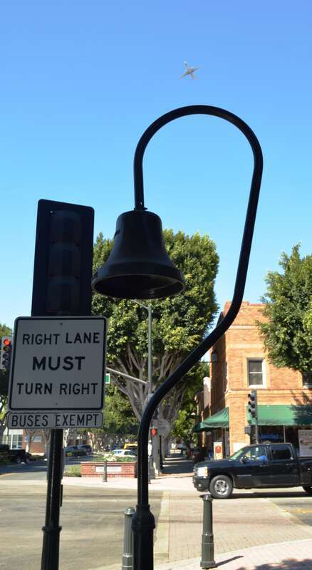 El Camino Real bell on the southeast corner of El Camino Real and Main Street in Old Town Tustin. The airplane is descending toward John Wayne Airport though seeing it from this angle may give the illusion that it's ascending.