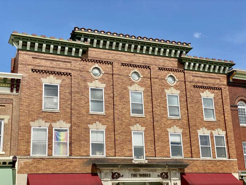 Built around the turn of the 20th Century, this Renaissance Revival-style building features an orange brick facade, divided into five bays by pilasters with brick corbeling above the third floor windows, stone window headers, a heavily bracketed
