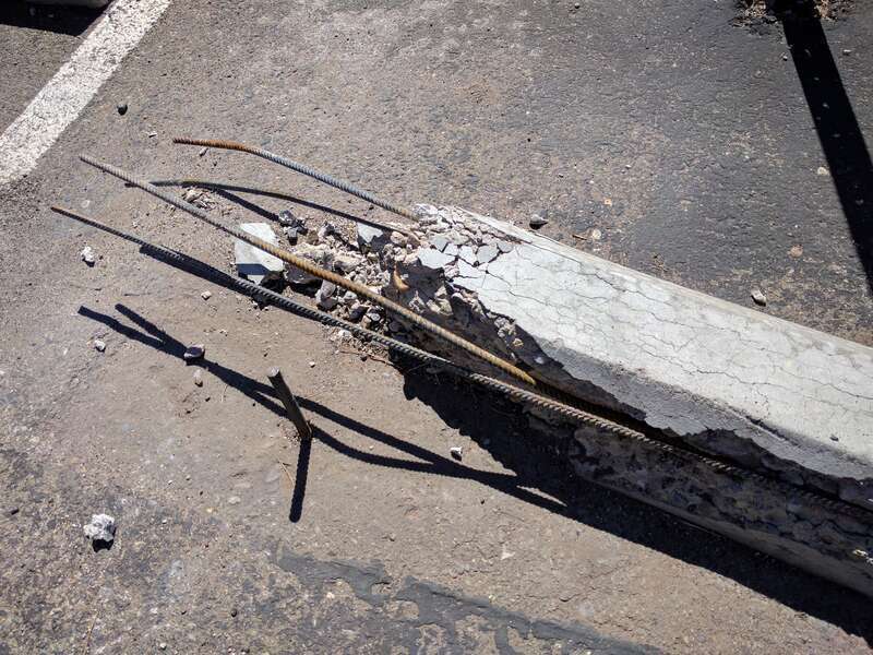 A parking chock at the end of a parking space in Santa Fe, New Mexico. It's been damaged, and the rebar reinforcing the chock is visible.