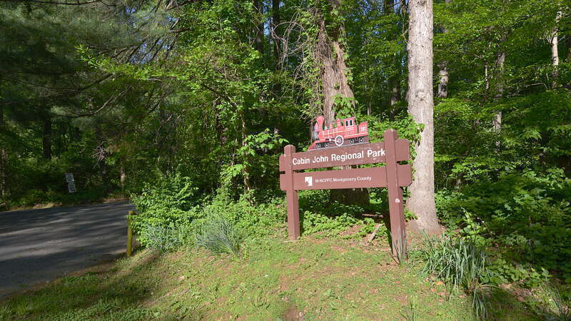 The entrance sign for the miniature train area of Cabin John Regional Park. The sign has a wooden train on it.  This park is operated by the Montgomery County Department of Parks. The entrance is on Westlake Drive.