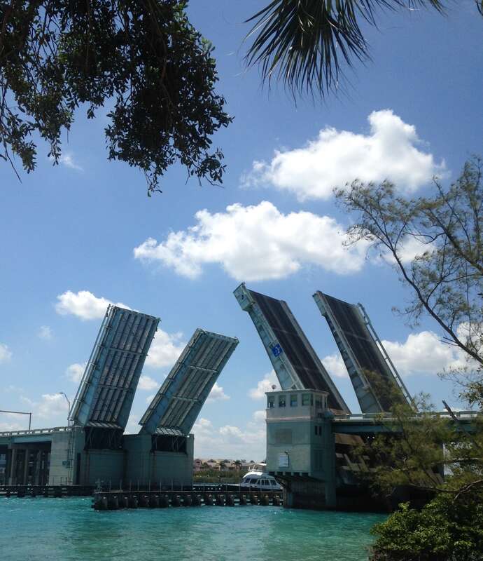 The Carlin White Bridge, also known as the Jupiter Federal Bridge, a pair of twin double-leaf bascule bridges over the Loxahatchee River in Jupiter, Florida, with the draw spans opened for a boat. It was built in 1958. This view is from the
