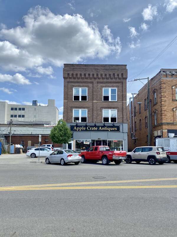 Built around the turn of the 20th Century, this building features a brown brick facade, paired one-over-one windows, stone belt coursing, brick cobbling, a rooftop parapet, a modified first floor retail shopfront, a low-slope shed roof, and an entry