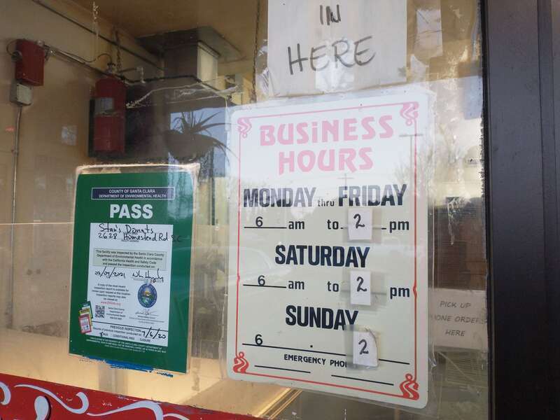 Signs affixed to the door of Stan's Donuts in Santa Clara, California, indicate a passing rating from the Santa Clara County Department of Environmental Health and the current business hours.