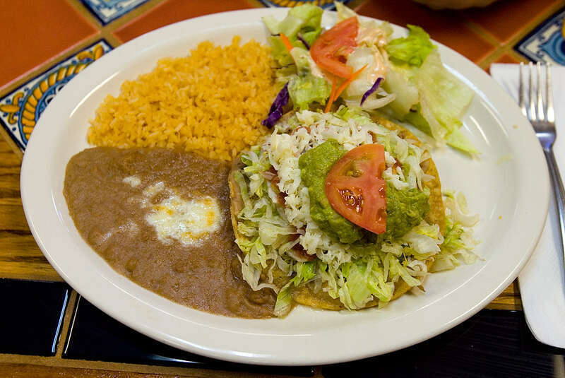 A beef tostada on a plate with refried beans, rice, and a salad as served by Los Compadres Mexican Restaurant at 944 C Street in Hayward, California, USA.  The photographer describes the scene as: &quot;A crispy flat corn tortilla shell topped with beef,
