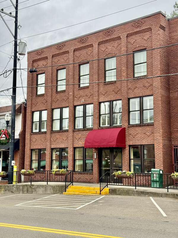 Built in the early 20th Century, this three-story commercial building features a red brick exterior, one-over-one windows, brick pillars on the front facade, decorative patterned brickwork and brick corbeling, and a low-slope roof enclosed by a