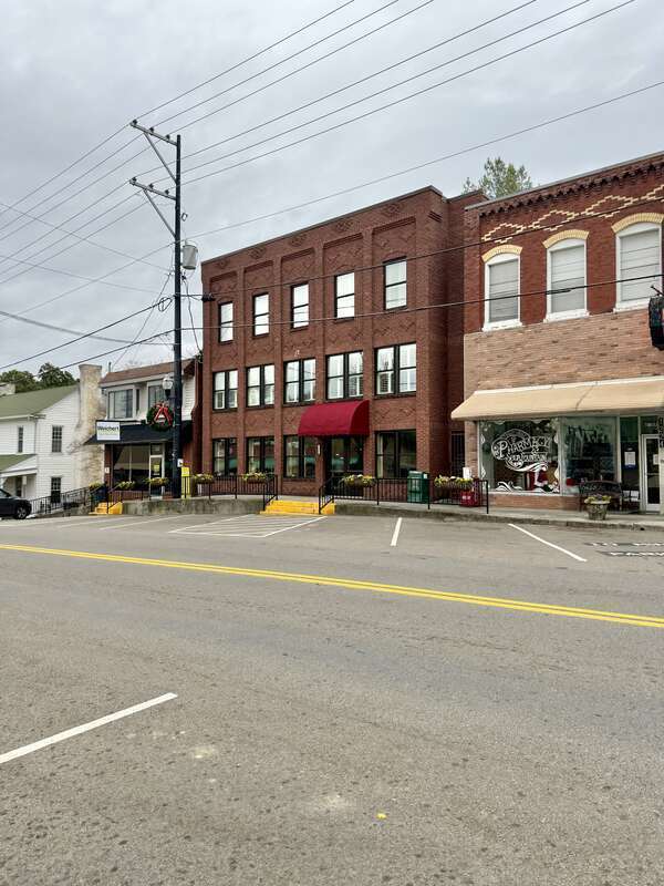 Built in the early 20th Century, this three-story commercial building features a red brick exterior, one-over-one windows, brick pillars on the front facade, decorative patterned brickwork and brick corbeling, and a low-slope roof enclosed by a