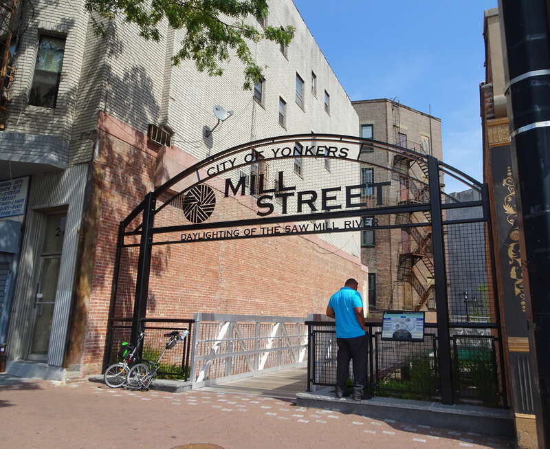 Looking east from Wharburton Avenue at Mill Street Plaza entralnce on a mostly sunny midday.