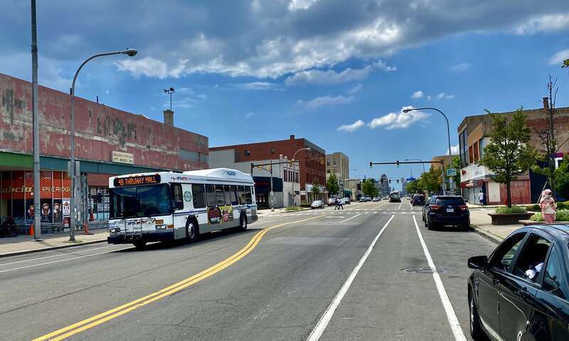An outbound NFTA Metro Bus #4 passes by the Broadway Market on a June 2021 afternoon, speeding toward its terminus at the Thruway Mall Transit Center. The Broadway Market, with its façade under restoration, is seen at left.