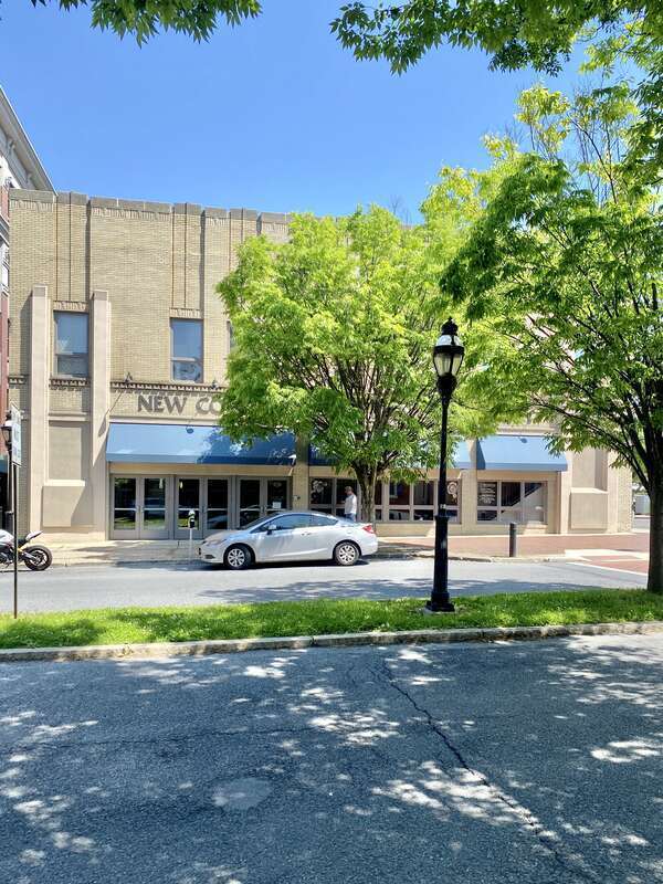 Built in the early 20th Century, this Art Deco-style building features a buff brick front facade and stucco-clad sides, stone trim, recessed panels above the window openings, decorative trim above the windows and below the parapet cap, decorative