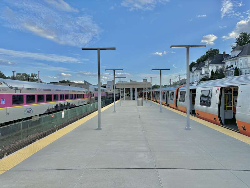 Looking south on the Orange Line platform at Oak Grove station in July 2024. On the left is an outbound Haverhill Line train to Reading; on the right is a 1400-series Orange Line train.