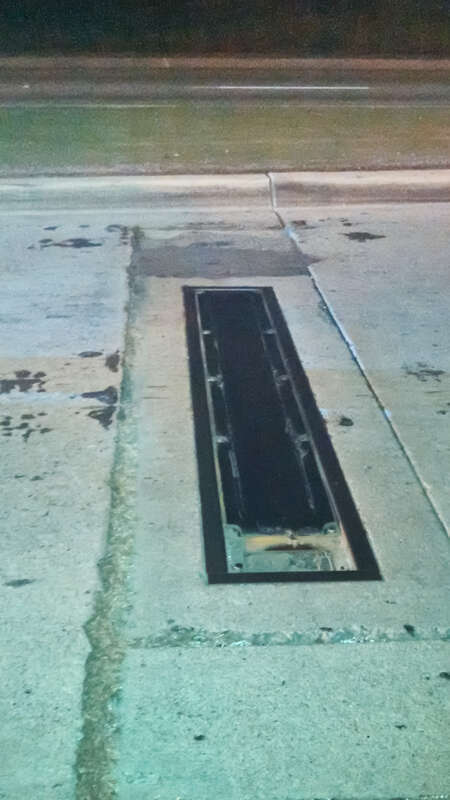 This is an older style of traffic detector. The wheels of the vehicle go over the treadle, which then makes the two metal plates inside contact each other, thus telling the traffic signal that a vehicle is at the intersection. The treadle is covered