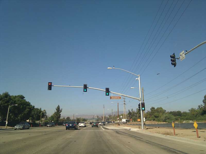 Photograph of the intersection at Jeffrey Road and Smoketree in Irvine, CA, facing north. The traffic light is visible, which is currently green for going straight and red for turning left. To the right is a field.