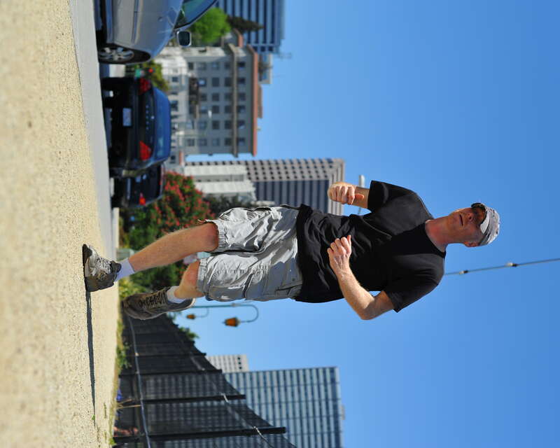 Jogging in street clothes, this jogger wears a color coordinated outfit:  gray Puma grunged out cap, black t-shirt, light gray cargo shorts, white socks and gray running shoes.
