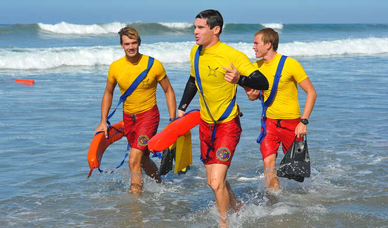 The center lifeguard leads the charge onto the beach. His buddy to the left listens to him while a third lifeguard observes a temporarily abandoned rescue tube floating nearby.

NCB_5513_cr