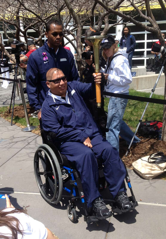 Retired U.S. Navy Boatswains Mate 1st Class Jim Castaneda, seated, accompanied by Hospital Corpsman 3rd Class Angelo Anderson, carries the torch during the opening ceremony for the 2013 Warrior Games in Colorado Springs, Colo., May 11, 2013. The