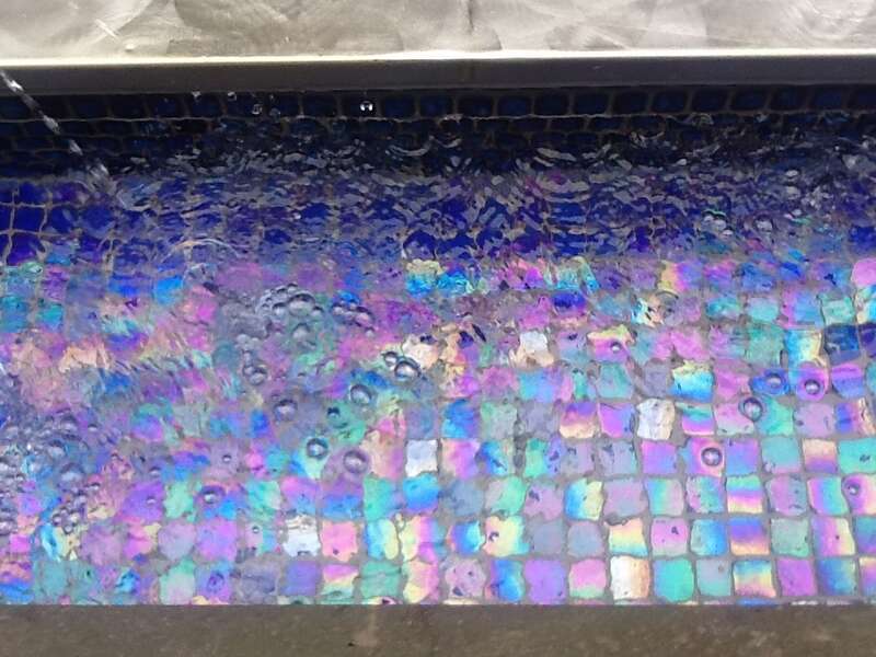 Detail of the fountain in the inner courtyard of the Aquila Court Building, now known as the Magnolia Hotel. Multicolored stones glow under the rushing water of the fountain.