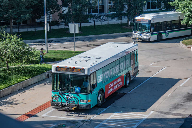 Capital Area Transportation Authority bus #636 at the CATA Transportation Center in East Lansing, Michigan in 2021. This bus is wrapped with graphics promoting COVID vaccines. The roof of the bus is still numbered 2719, the fleet number of this bus